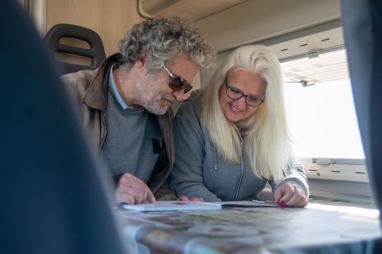 Smiling senior couple reviewing travel plans inside their cozy motorhome, symbolizing adventure and leisure.