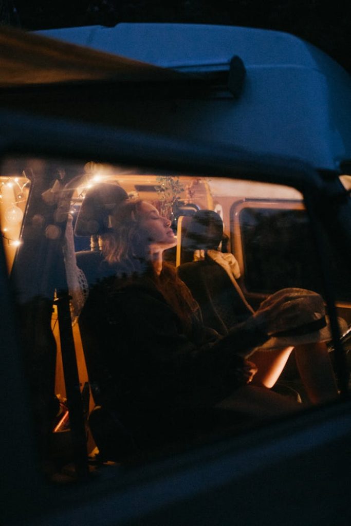 Woman relaxing inside a retro camper van during dusk, evoking a warm, serene atmosphere.